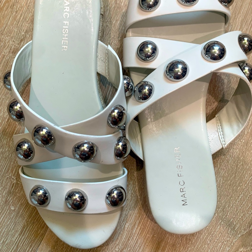 White sandals with circle silver metal accessories. Straw border around shoe.